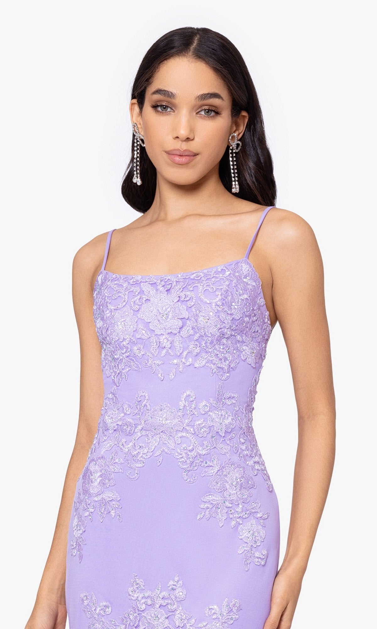 A woman wears the Blondie Nites Lilac Purple Long Prom Dress 4706BN, featuring thin straps and floral details, paired with long dangling earrings.